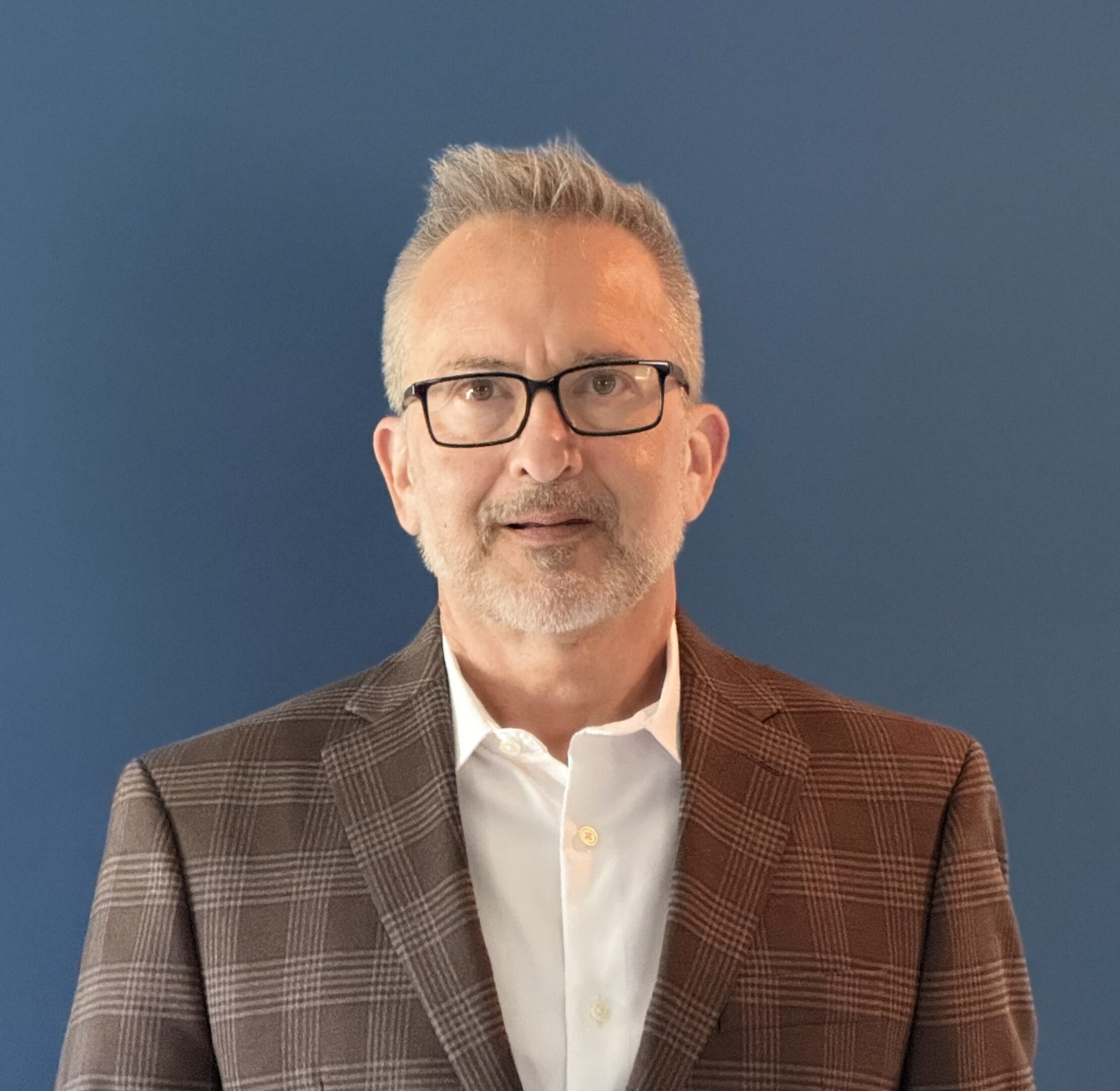 Mature man in glasses and plaid blazer against blue background.
